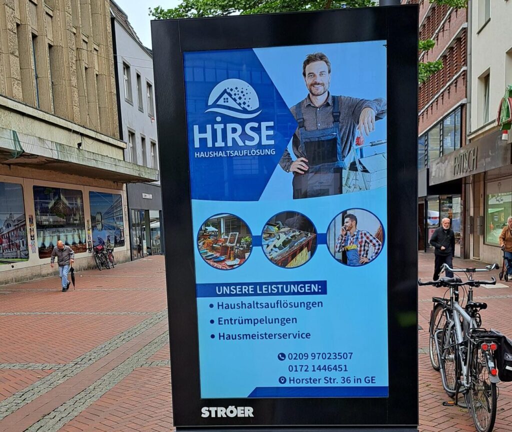 Geschäftsanzeige für "Hirse" mit lächelndem Mann in blauer Arbeitskleidung, Fahrräder im Hintergrund.