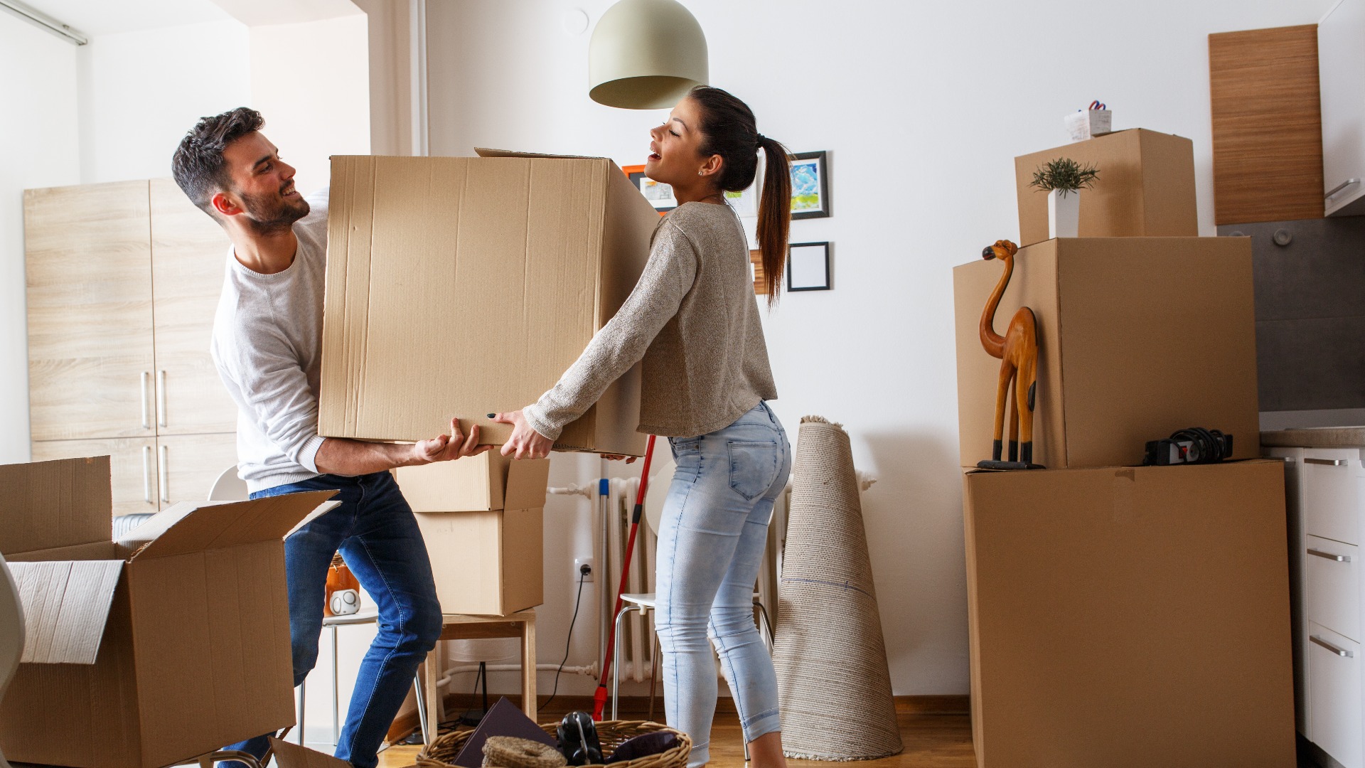 Young married couple carrying big cardboard box into new home. Moving house.